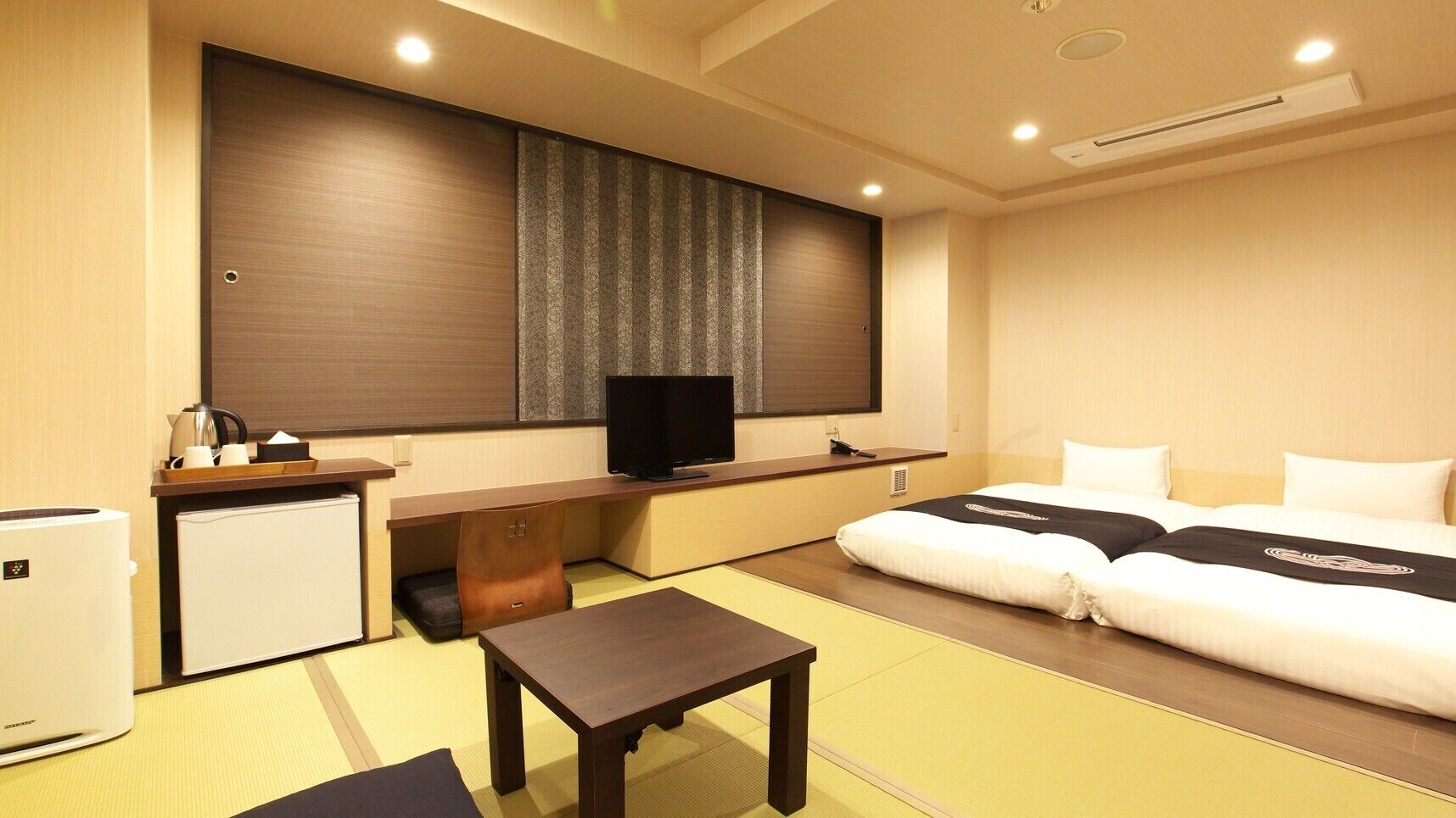 Habitación de hotel con cama, escritorio, televisión, refrigerador pequeño y sofá cama.