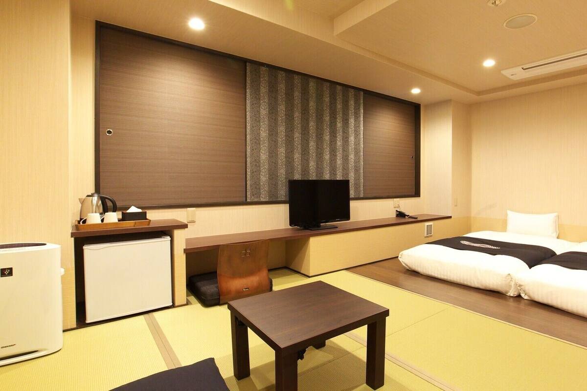 Quarto de hotel com cama, escrivaninha, televisão, pequeno frigorífico e futon.