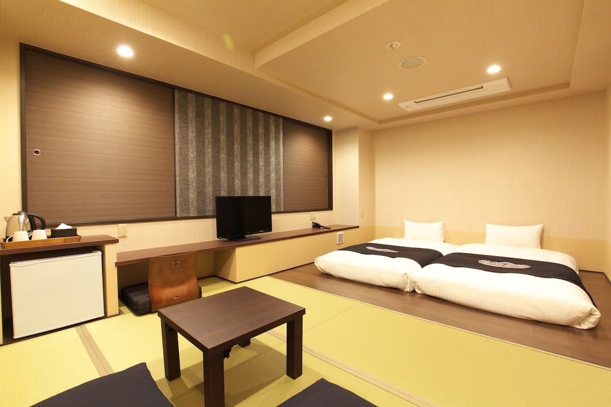 Quarto de hotel com cama, escrivaninha, televisão e um pequeno frigorífico.