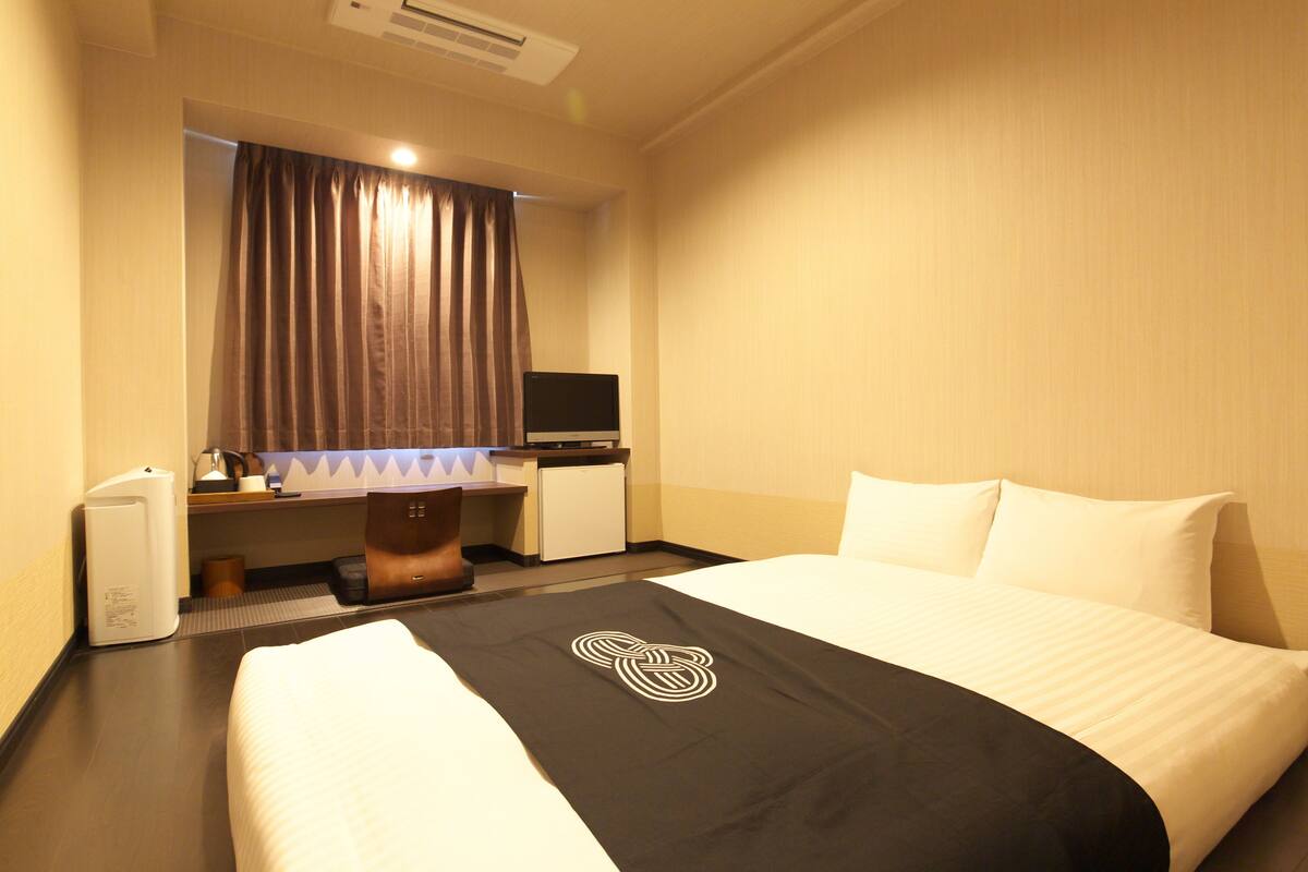 Quarto de hotel com cama, secretária, computador e máquina de café.
