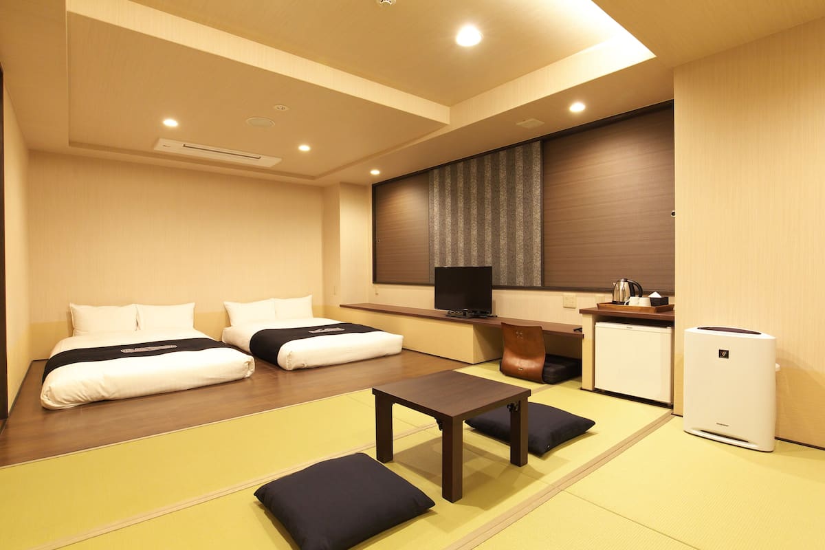 Quarto de hotel com duas camas, uma mesinha, televisão, frigorífico e um futon.