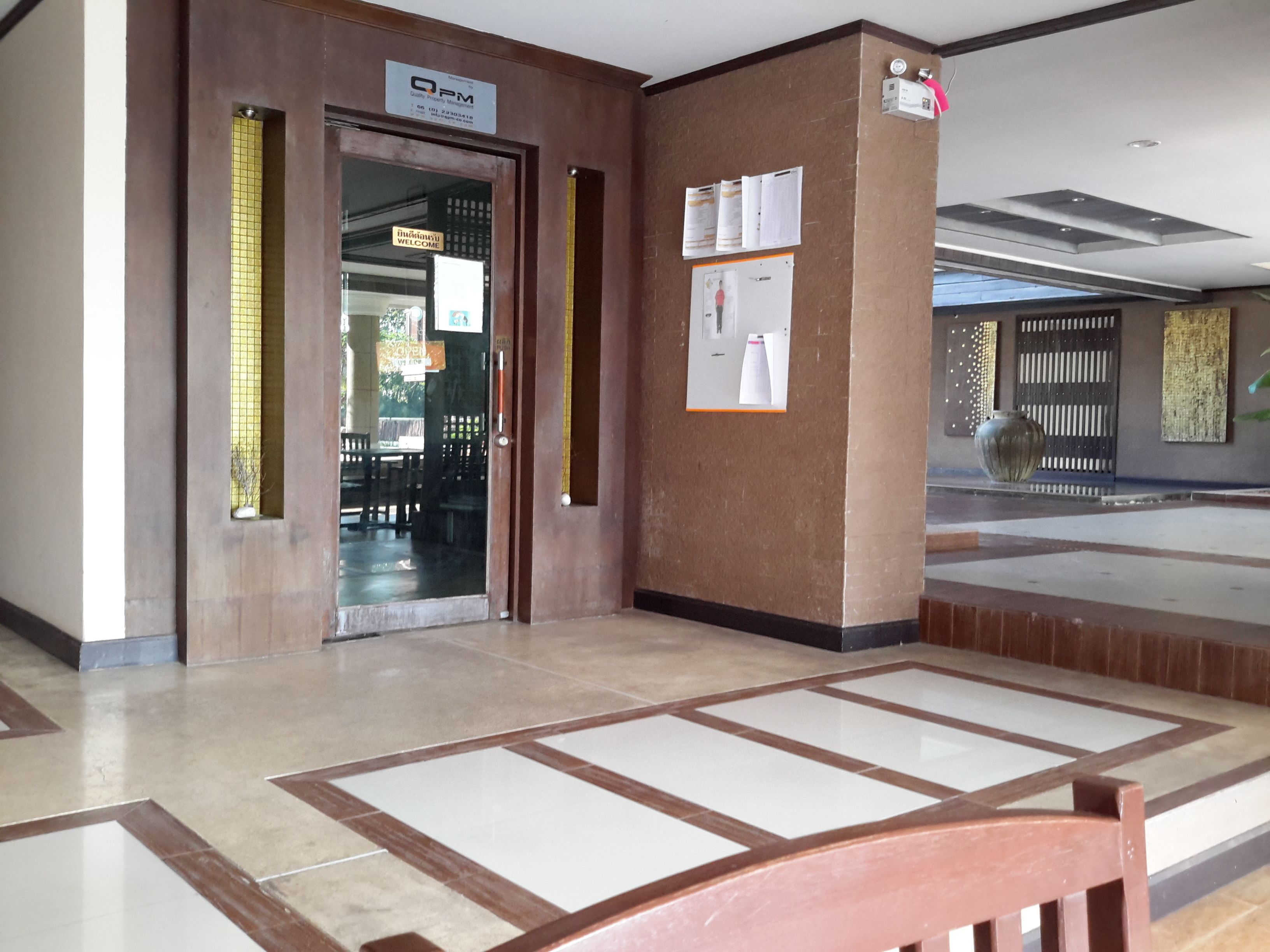 A lobby with a reception desk, a glass door entrance, and a bulletin board on the wall.