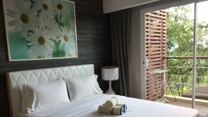 A hotel room with a large bed, a painting of daisies, a window with a view of greenery, and a nightstand with a lamp. - Beachfront Family Penthouse Hua Hin (Hua Hin)