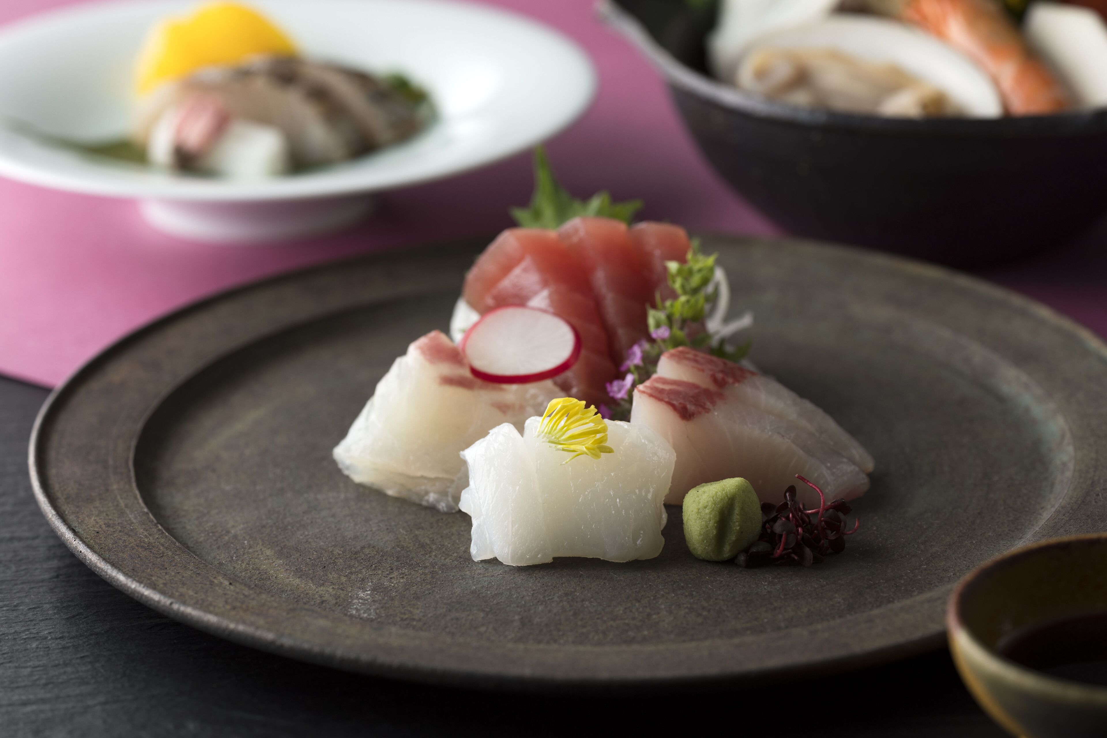 Un plato de sashimi con guarniciones sobre un plato oscuro.