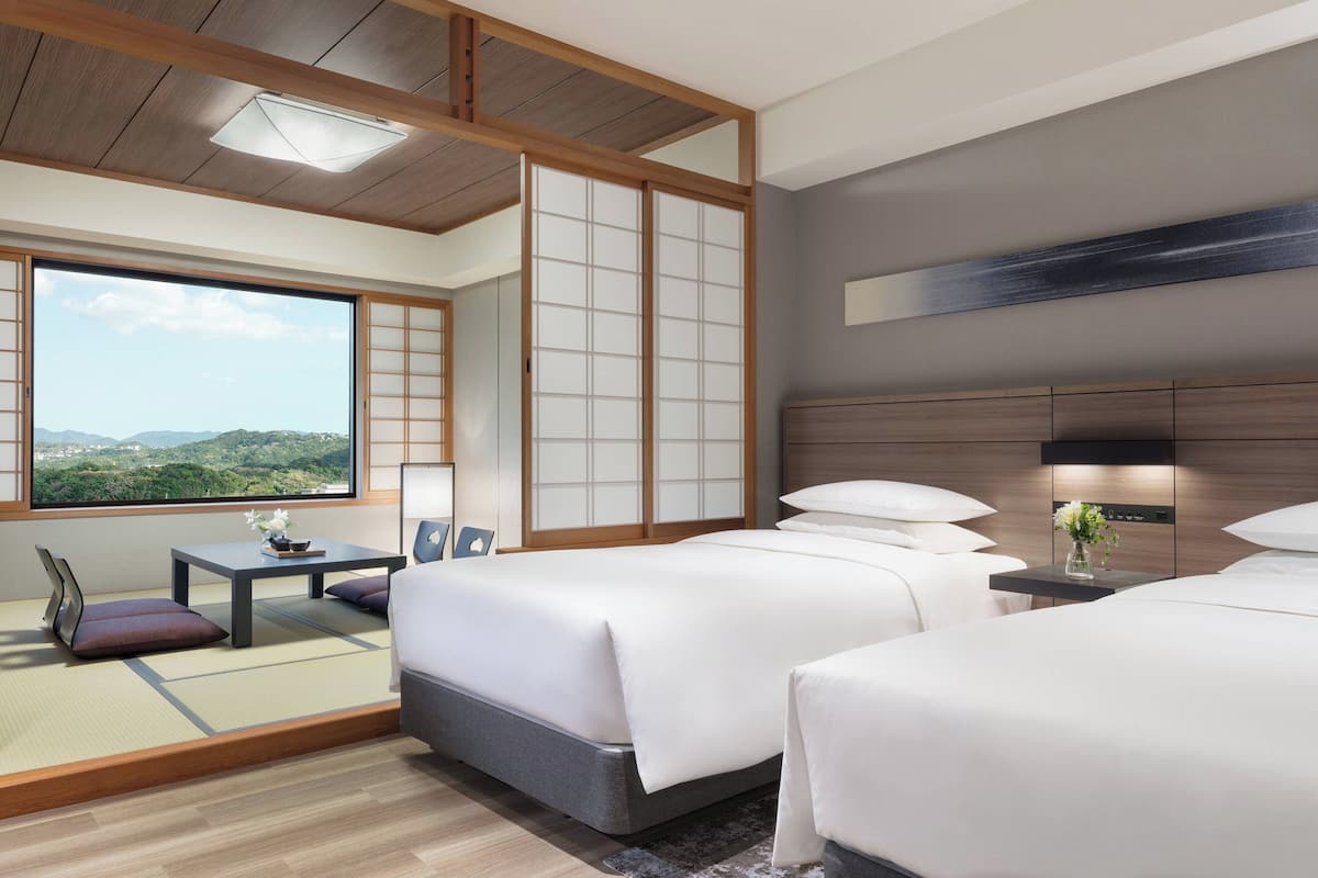 Een moderne hotelkamer met twee bedden, een klein tafeltje met een lamp en uitzicht op het groen.