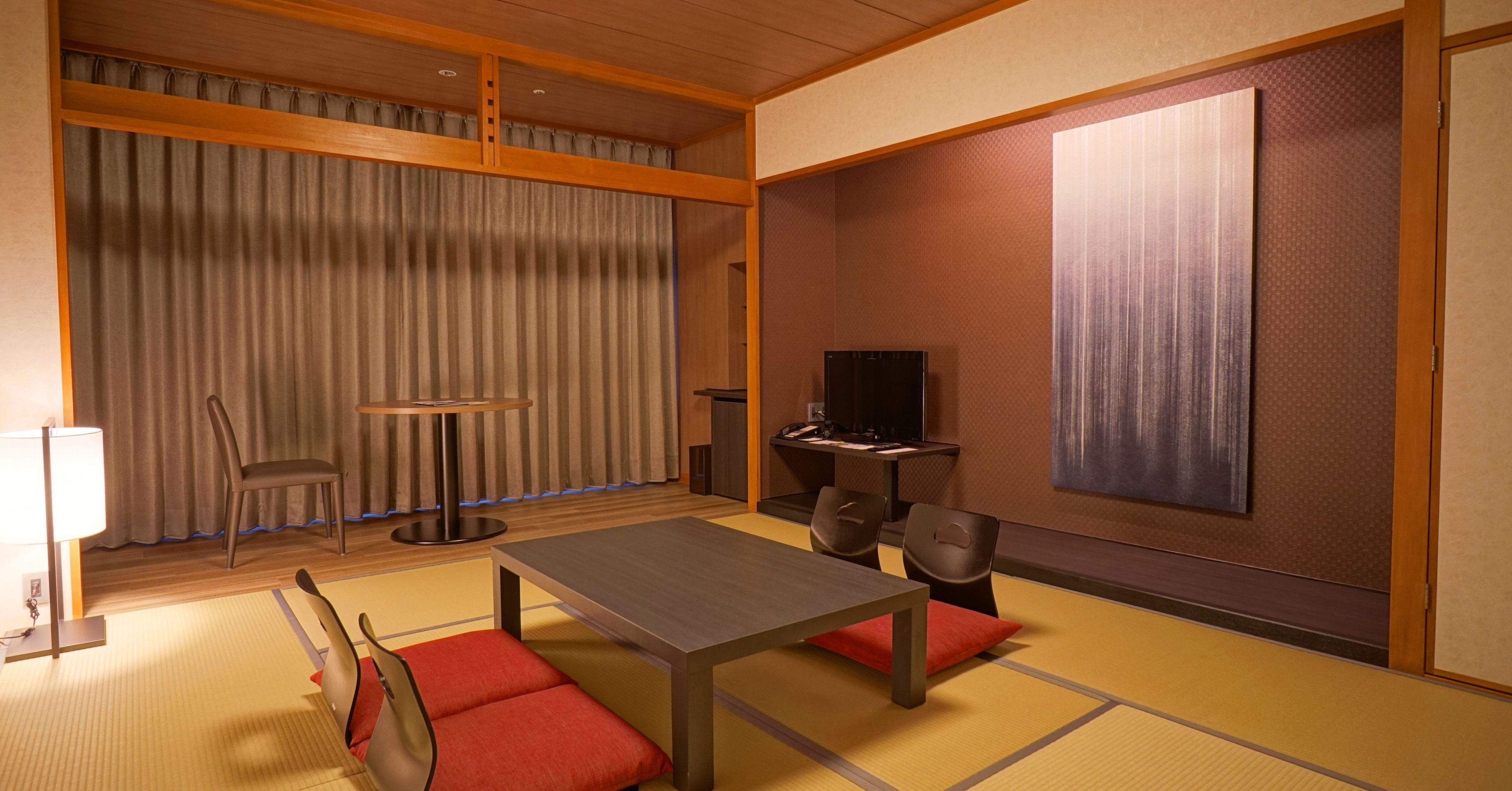 A traditional Japanese room with tatami flooring, a low table, chairs, a television, and a large painting on the wall.