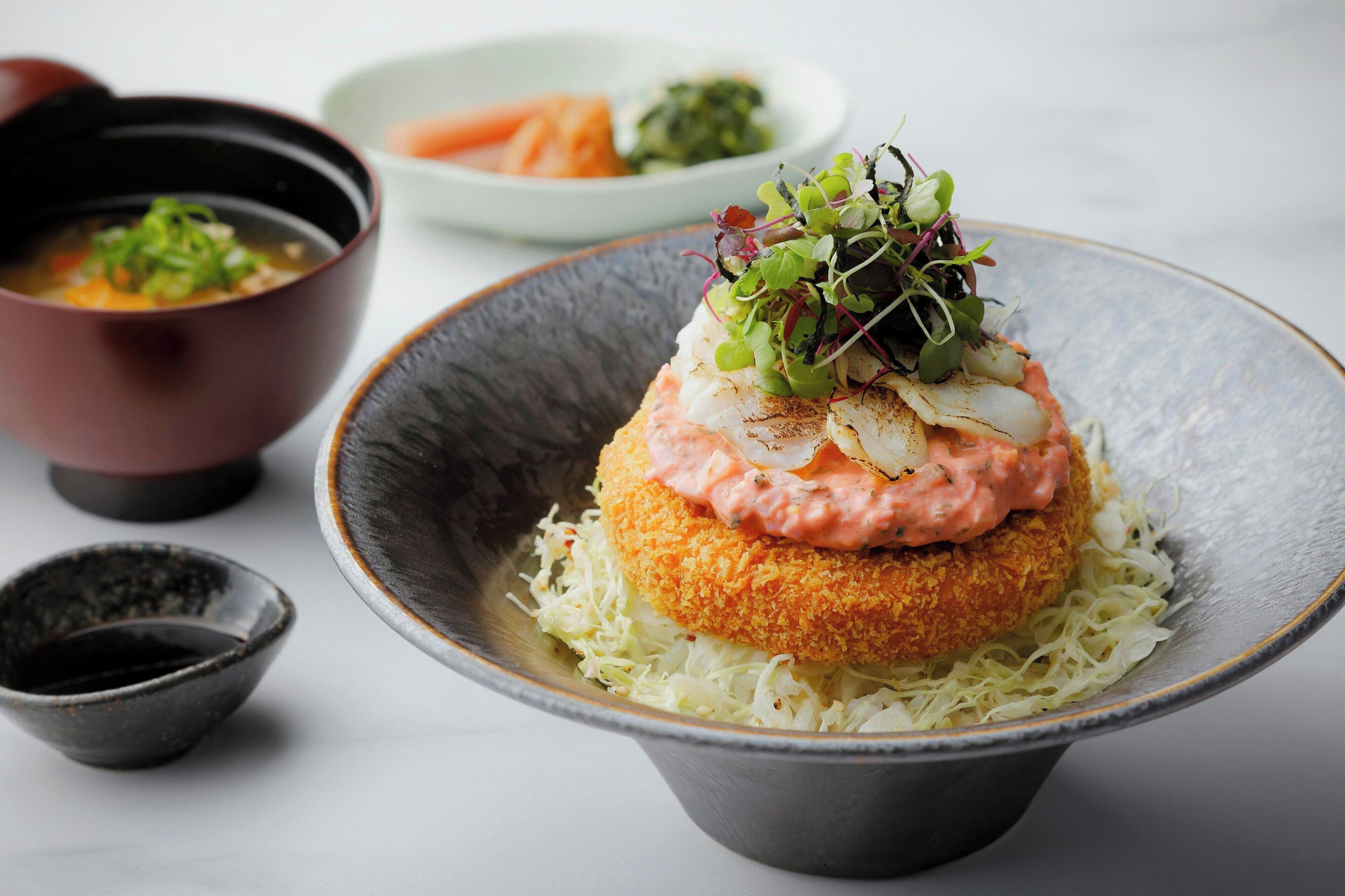 A bowl of food with a crispy base, topped with a creamy sauce and greens.