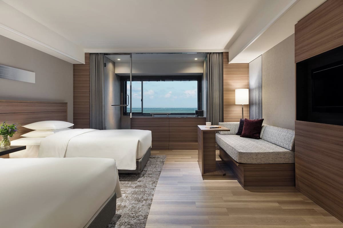 Een moderne hotelkamer met twee bedden, een bank, een televisie en een groot raam met uitzicht op zee.