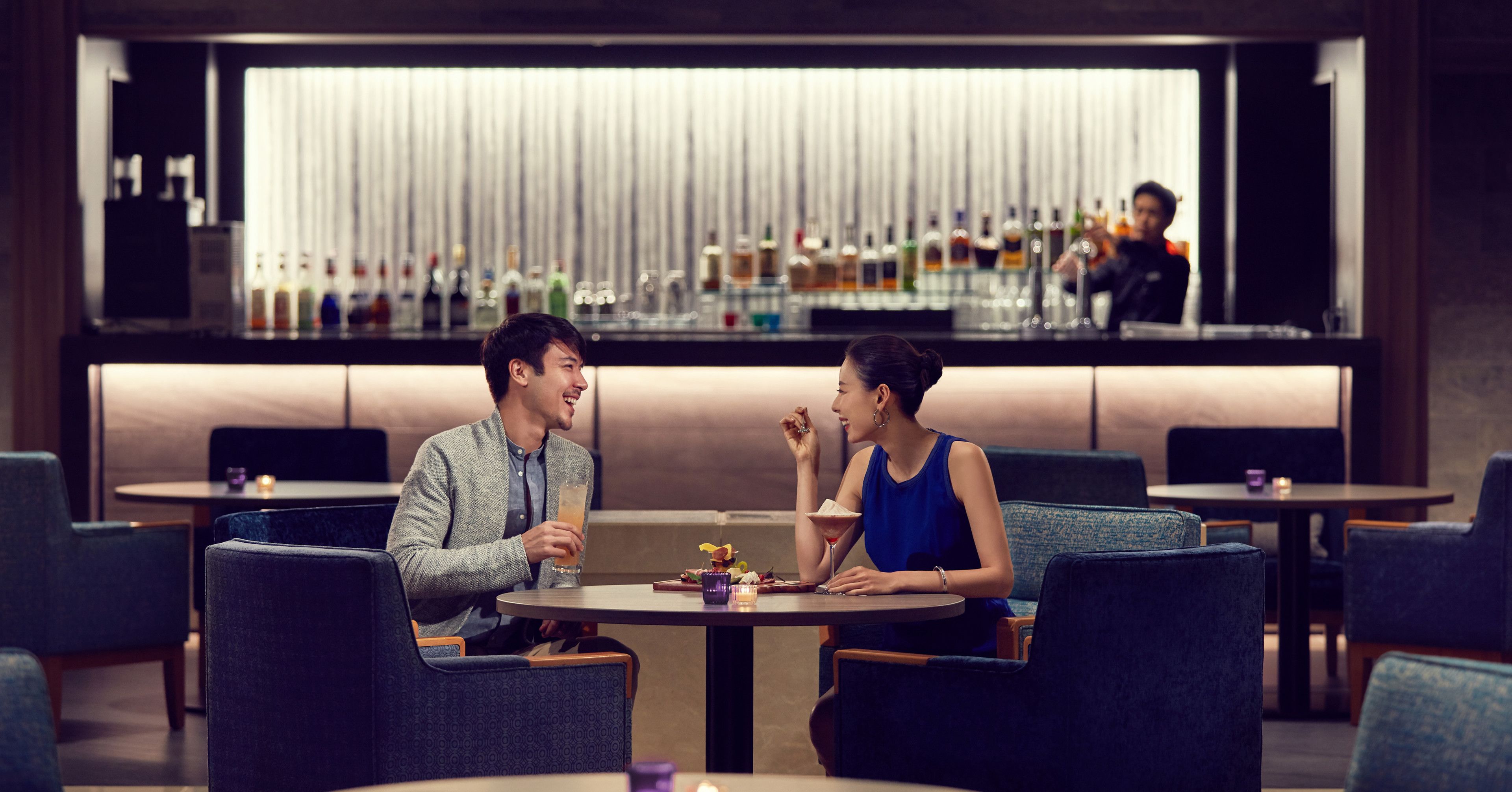 A couple dining at a round table in a modern restaurant with a bar in the background.