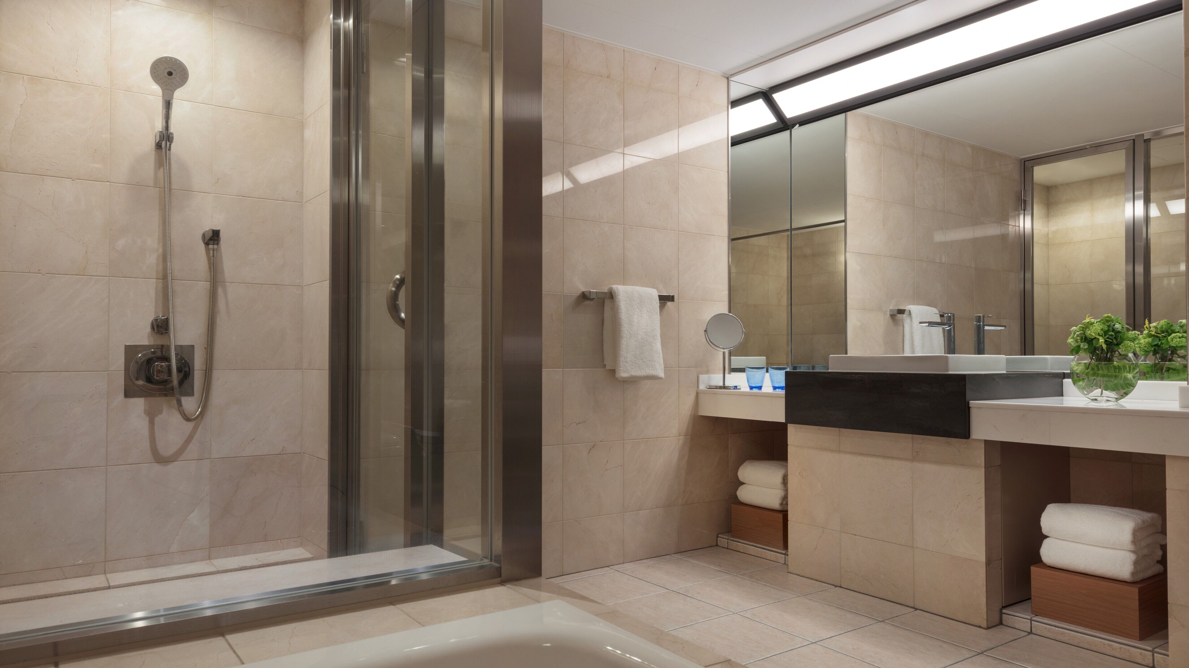 A modern bathroom with a glass-enclosed shower, a large mirror, and a vanity with a sink and countertop.