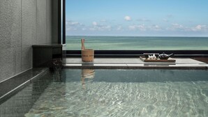 On peut clairement voir une piscine avec vue sur l’océan, un plateau en bois avec un service à thé et un petit seau.