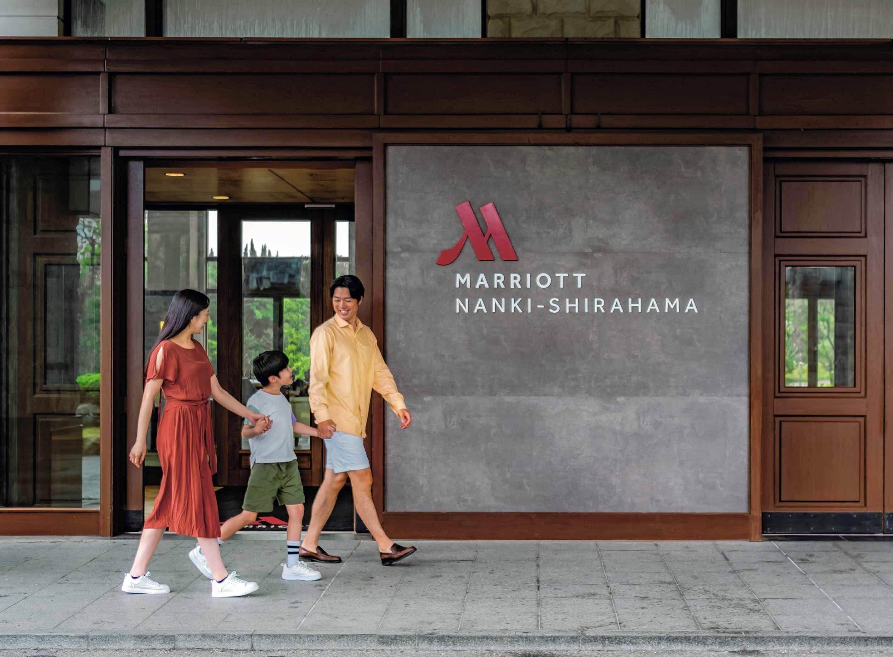 Una familia caminando hacia un edificio con un logotipo grande y el nombre 'Marriott Nanki-Shirahama'.