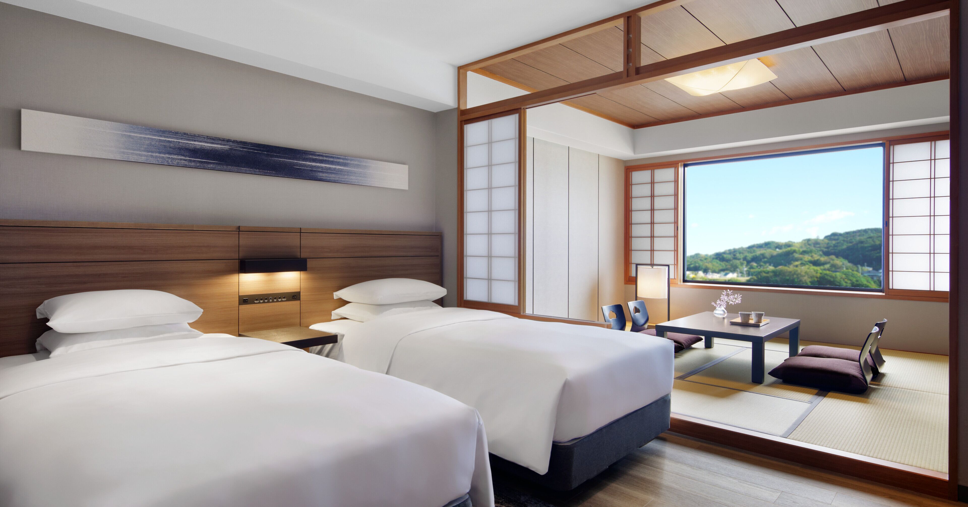 A hotel room with two beds, a desk, and a view of the outdoors.