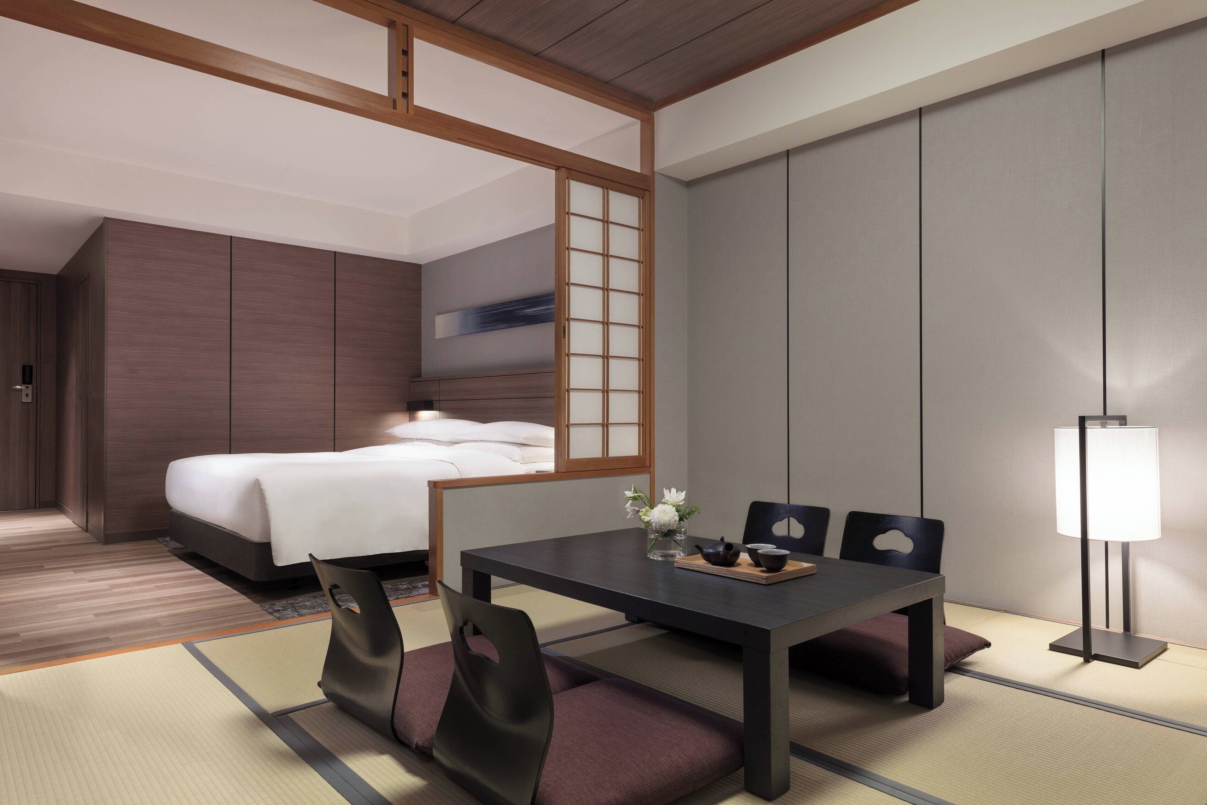 Habitación de hotel moderna con cama, una mesa de comedor con sillas, una lámpara y vistas a la ciudad.