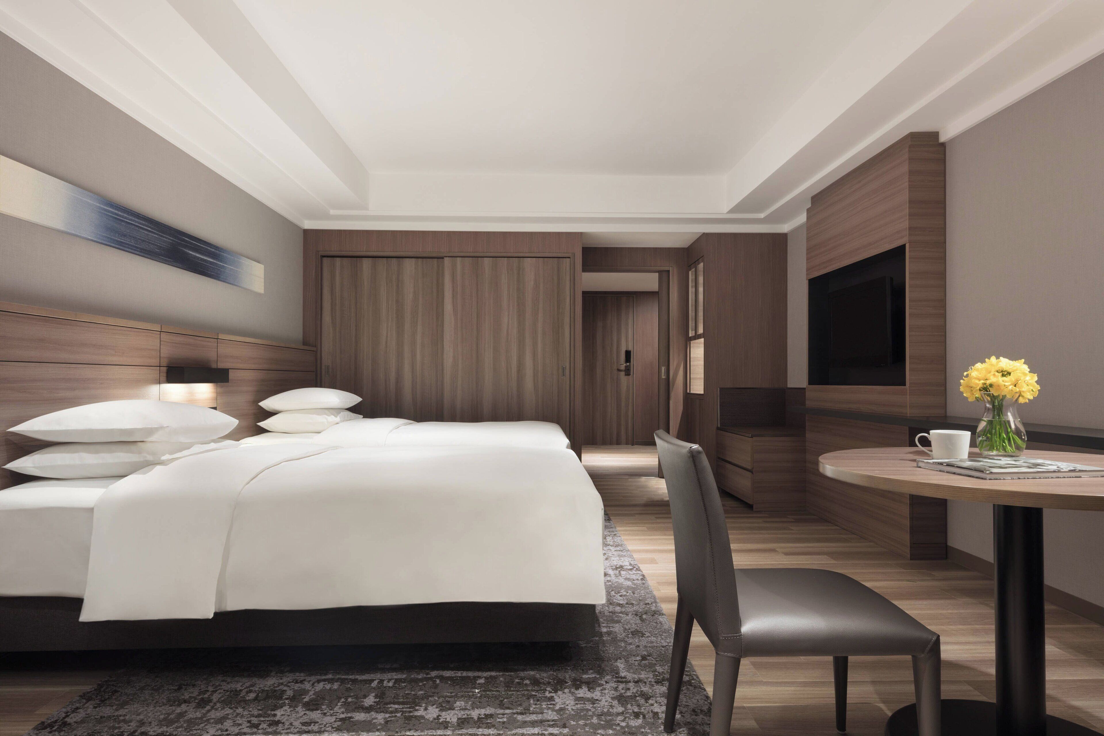 Habitación de hotel moderna con una cama grande, un escritorio con una silla, un televisor de pantalla plana y un jarrón con flores.