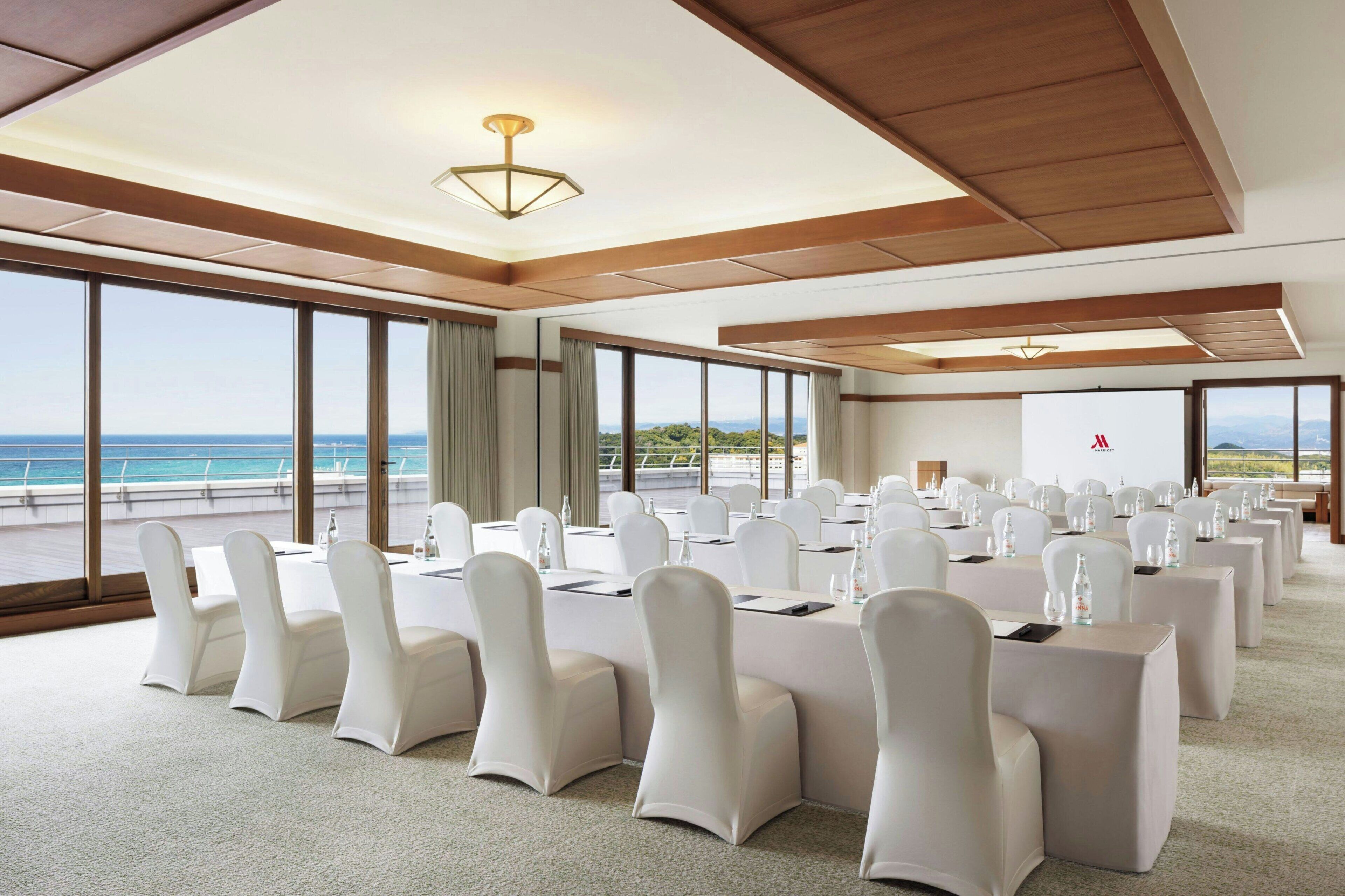 Un salón de conferencias con amplias ventanas, sillas blancas y mesas dispuestas para una reunión.