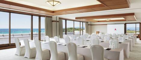 A conference room with large windows, white chairs, and tables arranged for a meeting.