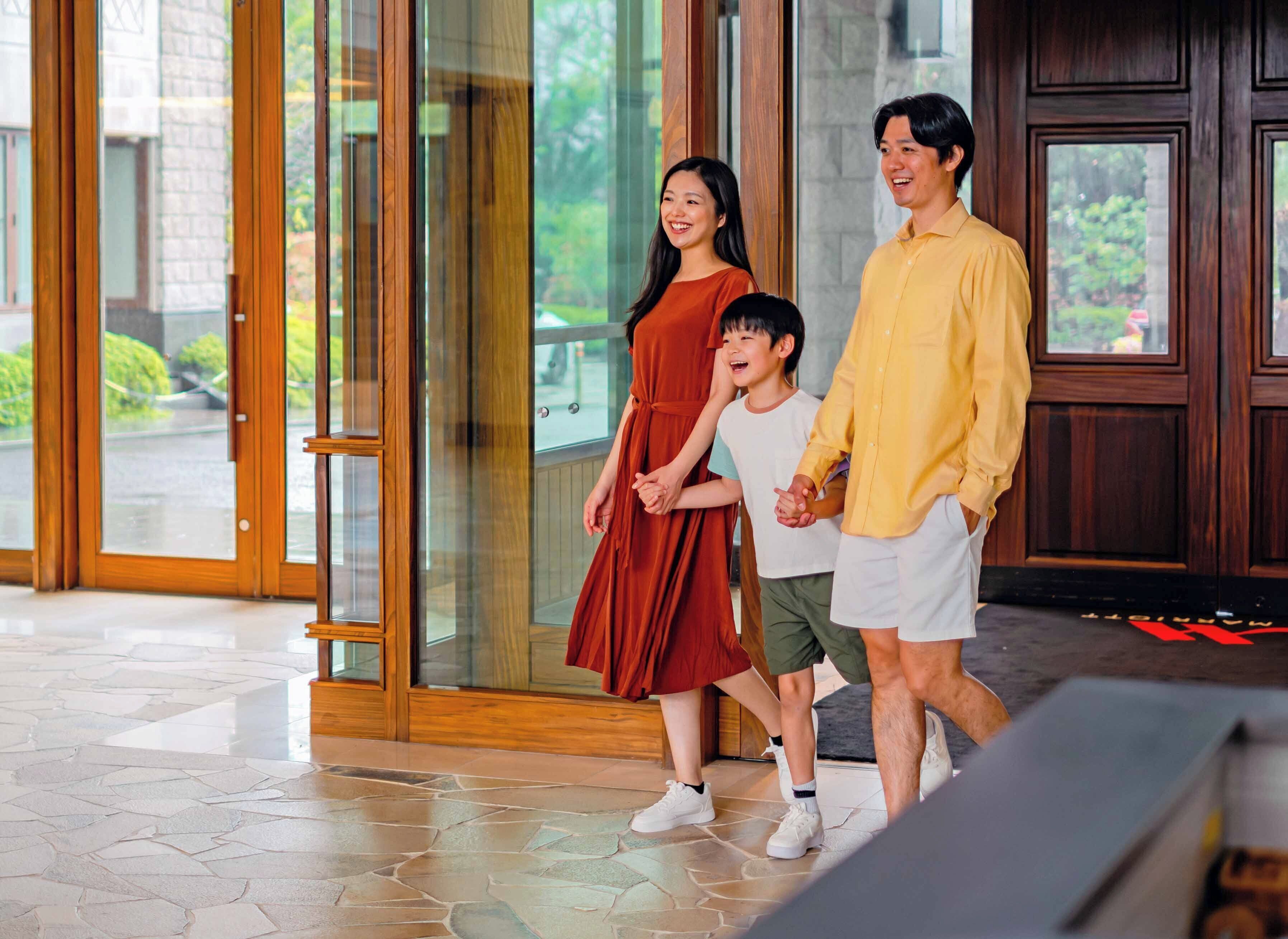 A family walking through a hotel entrance with glass doors and a stone-tiled floor.