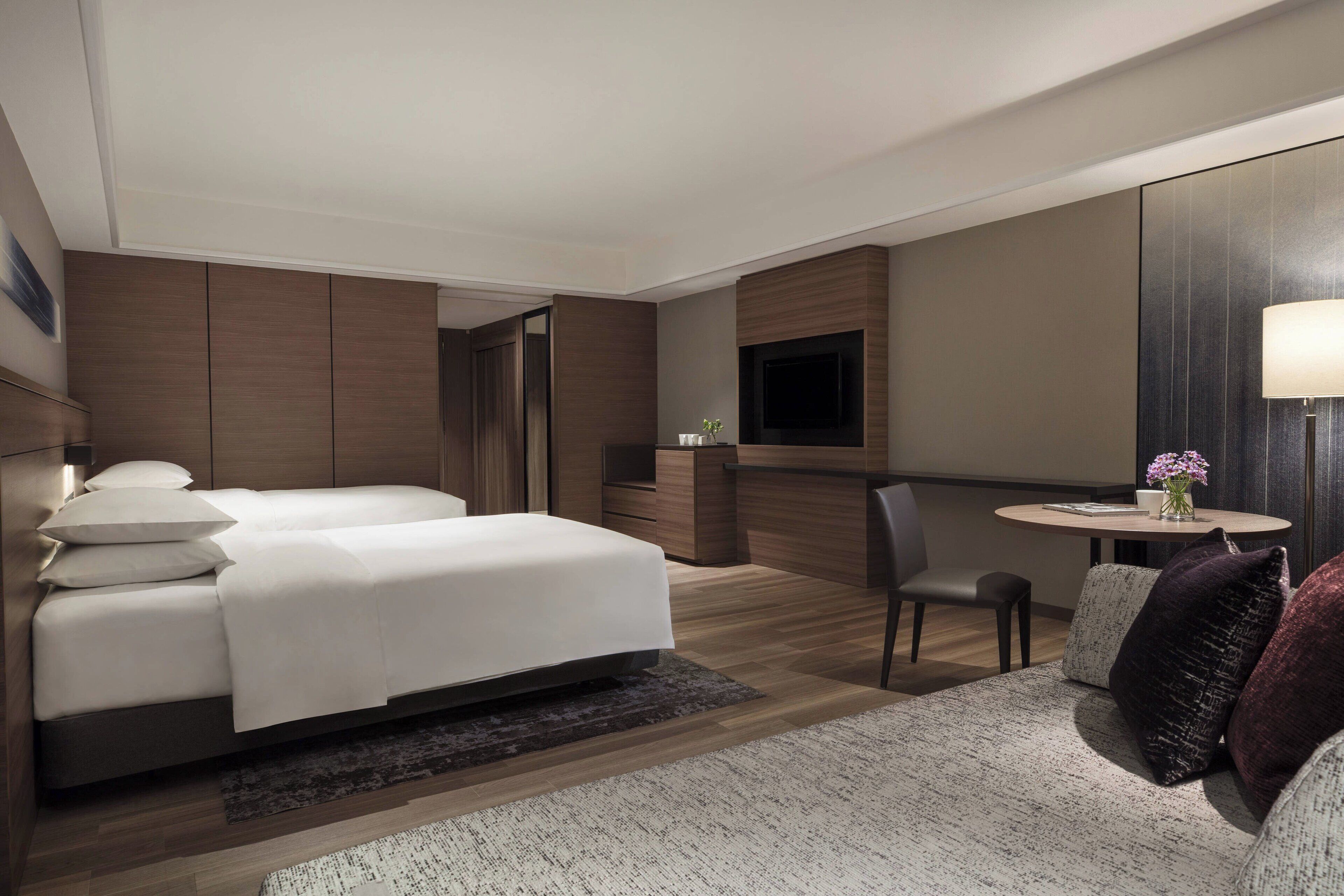 Een hotelkamer met een groot bed, een bureau, een stoel, een televisie en een kleine tafel met een bloevas.