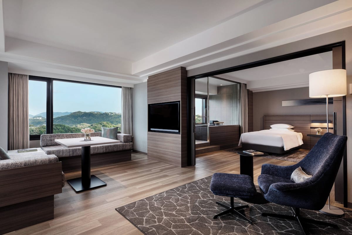 Een moderne hotelkamer met een groot bed, een zithoek met een bank en fauteuil, een flatscreen televisie en uitzicht op de omgeving.