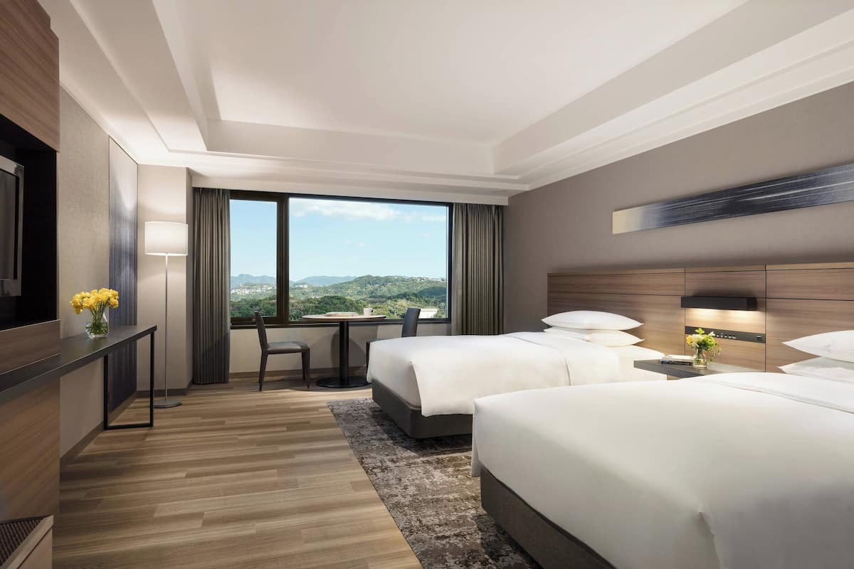 Een hotelkamer met twee bedden, een bureau en uitzicht op de bergen.