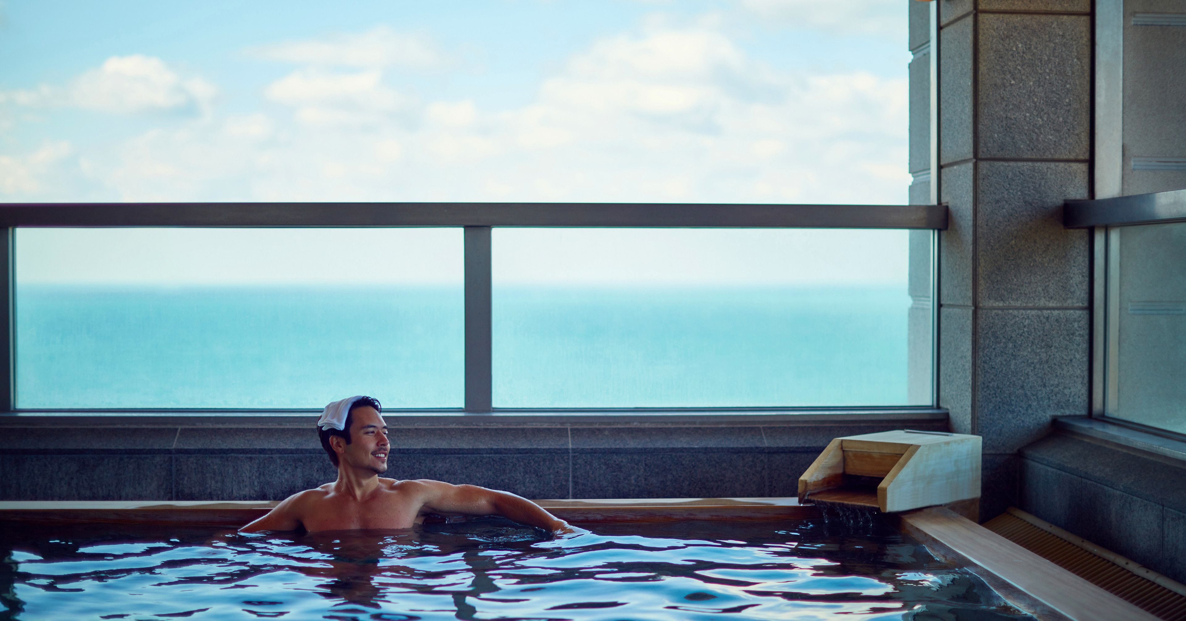 A man in a bathtub with a view of the ocean.