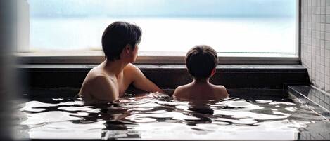Two individuals in a hot tub with a view of a body of water through a window.