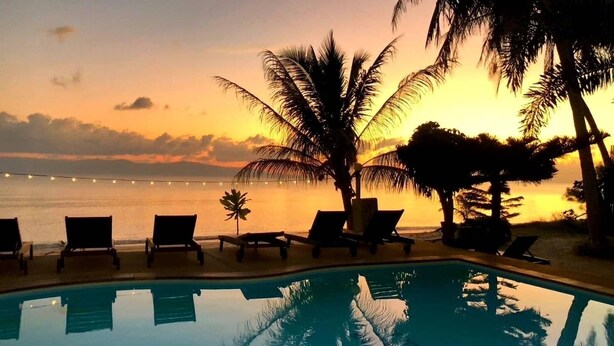 A poolside area with lounge chairs and palm trees, overlooking a body of water during sunset. - Phangan Lodge (Ko Pha-ngan)