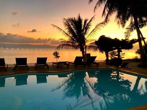 A poolside area with lounge chairs and palm trees, overlooking a body of water during sunset. - Phangan Lodge (Ko Pha-ngan)