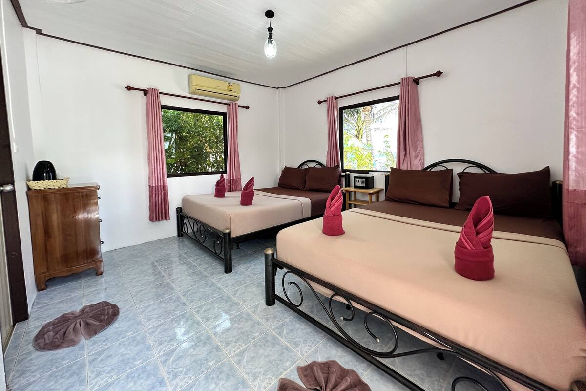 A hotel room with two beds, a wooden cabinet, an air conditioner, and a ceiling fan.