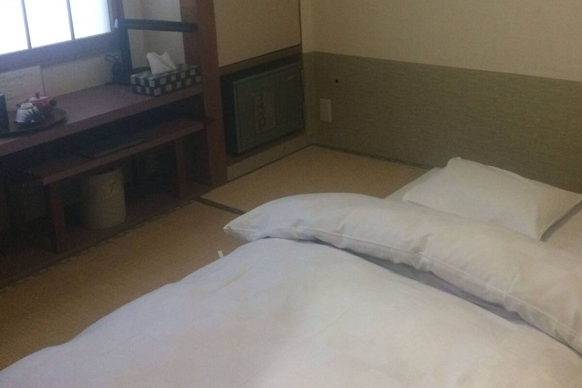 Habitación de hotel con cama, almohadas, una mesita con una caja de pañuelos y un cesto de basura.