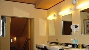 A hotel bathroom with two sinks, a clock, and a hairdryer on the wall.