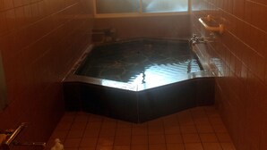 A small, dimly lit room with a hot tub, tiled walls, and a window with frosted glass.
