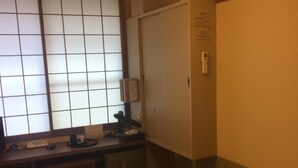 A traditional Japanese-style room with tatami flooring, a futon bed, a shoji screen, a desk with a lamp, and an air conditioning unit.