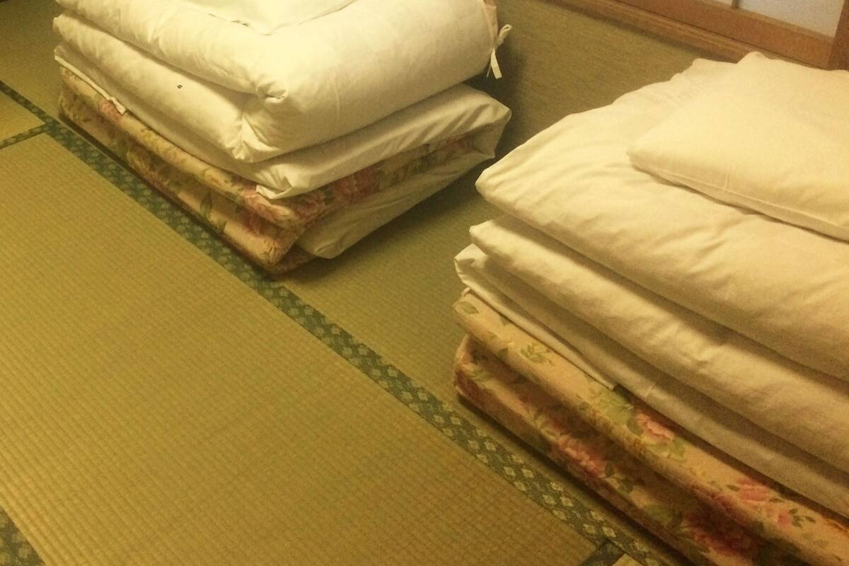 Una habitación con esteras tatami, con dos conjuntos de ropa de cama, uno estampado con flores y otro liso.