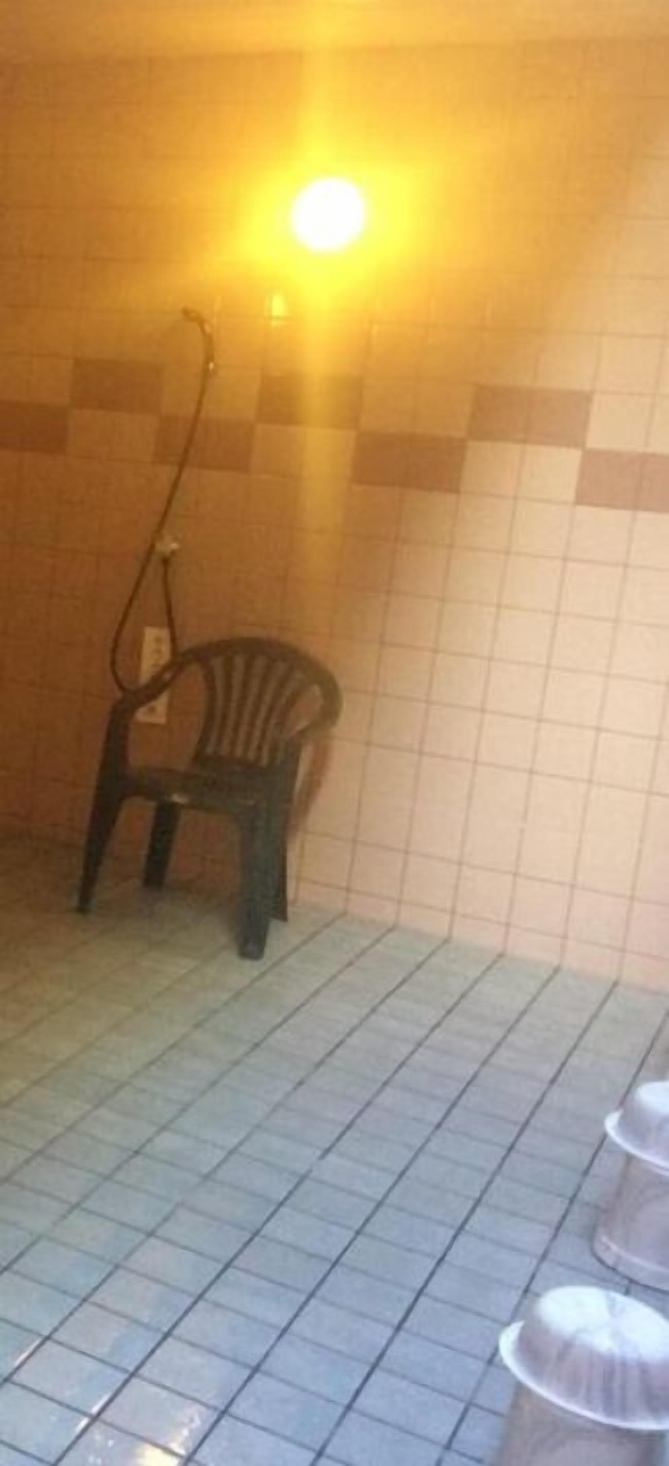 A tiled shower area with a plastic chair and a showerhead.