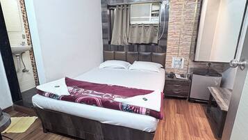 A bedroom with a bed, a bedside table, a mirror, a wall-mounted air conditioning unit, and a ceiling fan.