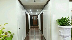 A hallway with a tiled floor, white walls, and a wooden door at the end. There are potted plants on either side of the hallway. - Hotel Mogul Palace (Mumbai)