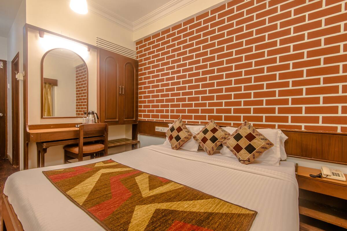 Habitación de hotel con pared de ladrillo, una cama con colcha estampada, un escritorio con silla, un espejo y un teléfono en una mesita de noche.
