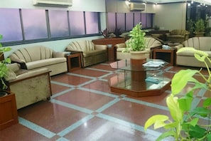 Un vestíbulo con piso de cuadros, varios sofás, una mesa de centro de vidrio y plantas en macetas.