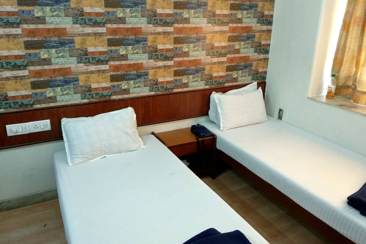 Habitación de hotel con dos camas individuales, cabecero de madera, pared estampada, mesita de noche con teléfono y ventana con cortinas.