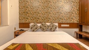 A hotel room with a large bed, a stone-patterned wall, wooden headboard, and a wooden nightstand with a phone. - Hotel Mogul Palace (Mumbai)
