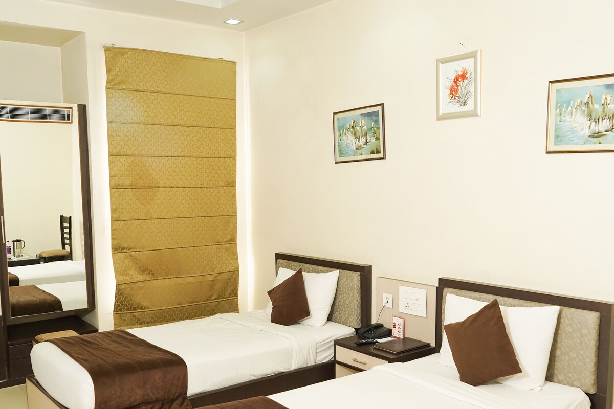 A hotel room with two single beds, a ceiling fan, a large mirror, and artwork on the walls.