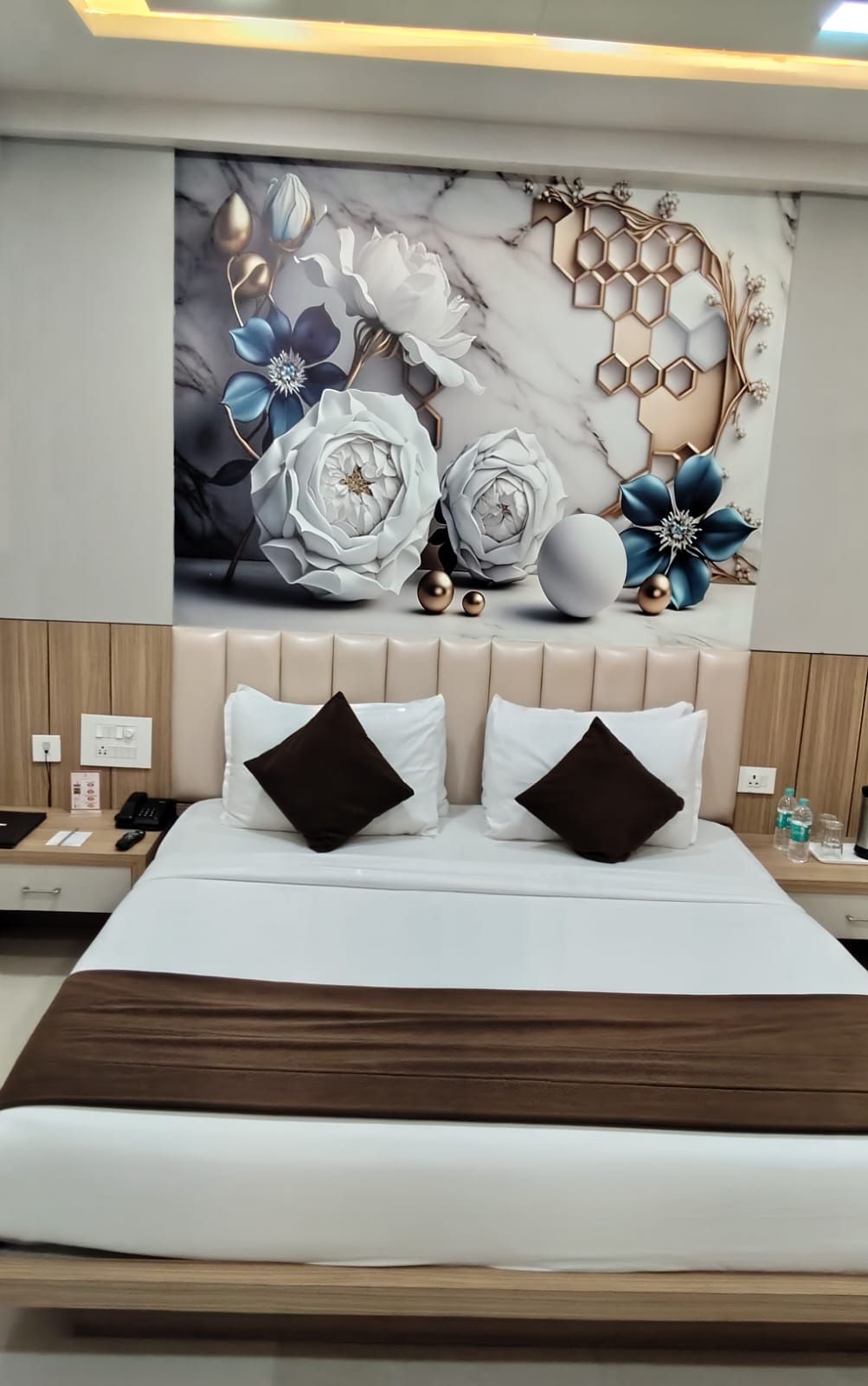 Une chambre d’hôtel avec un grand lit, deux oreillers, une table de chevet, un téléphone fixé au mur et un élément décoratif mural.
