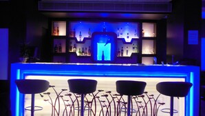 A bar area with a neon sign, shelves with bottles, and three bar stools. - Hotel Yash Regency (Jaipur)