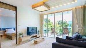 A modern hotel room with a bed, TV, wooden furniture, a balcony with chairs, and a large window. - Hua Hin Luxury Beachfront Condo By Mon (Hua Hin)