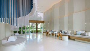 A modern interior with a curved seating area, a wooden table, and a large window offering a view of greenery. - Hua Hin Luxury Beachfront Condo By Mon (Hua Hin)