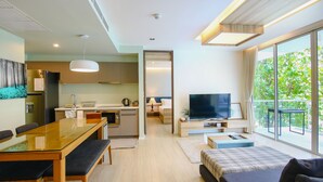A modern living room with a sofa, a TV, and a balcony with large windows. - Hua Hin Luxury Beachfront Condo By Mon (Hua Hin)