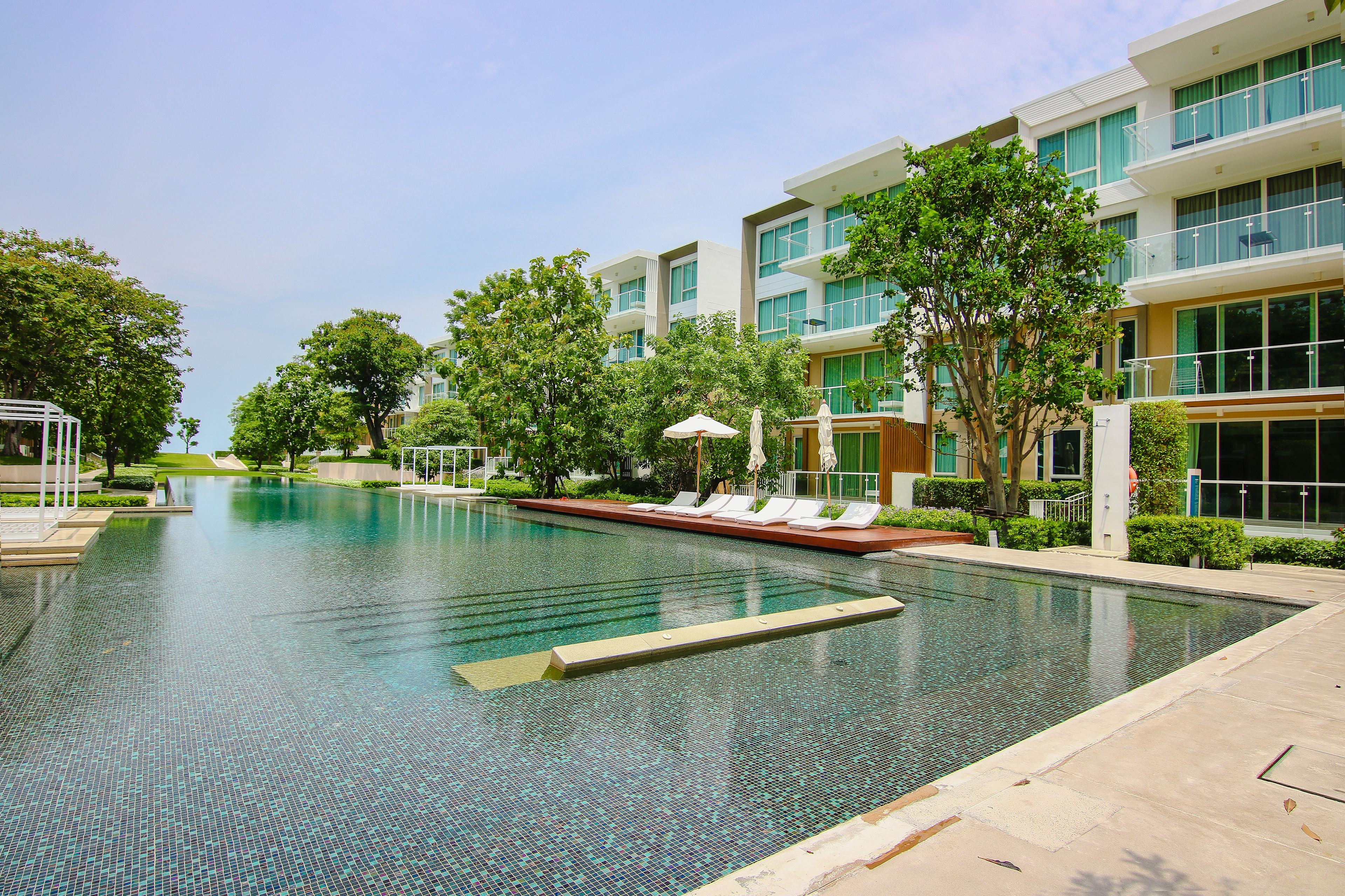 Un hotel moderno con una amplia piscina, mobiliario exterior y abundante vegetación.