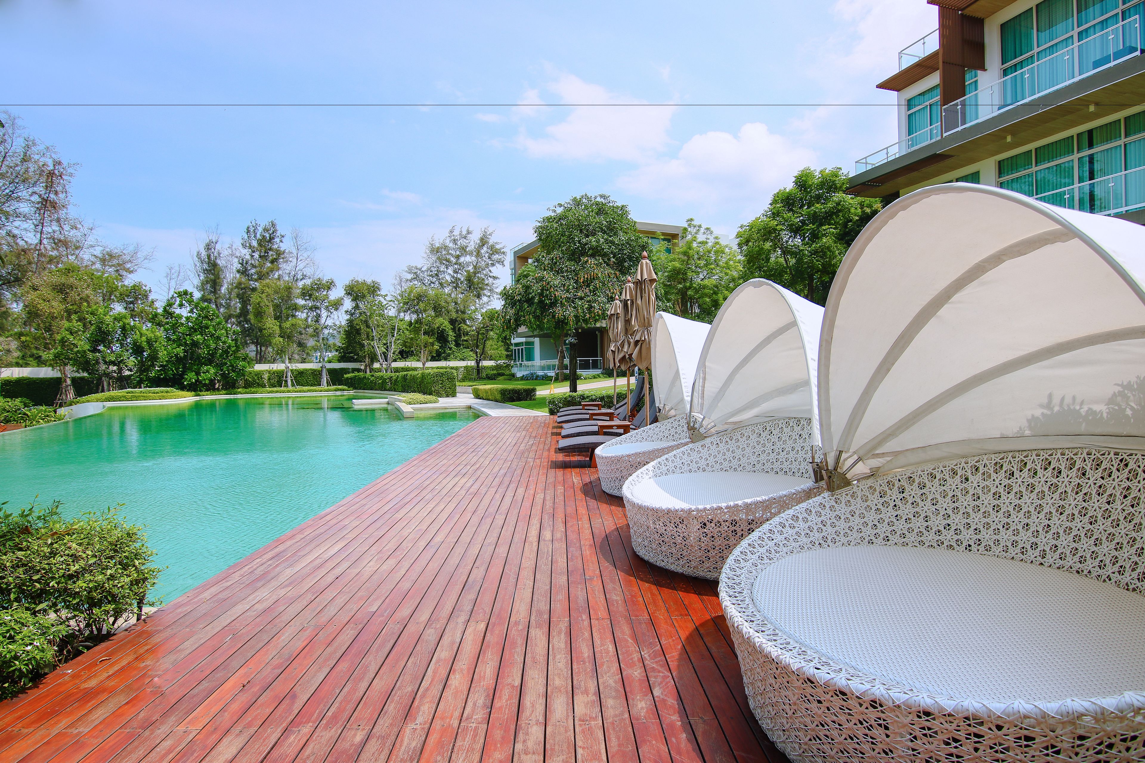 A poolside area with lounge chairs and umbrellas, a wooden deck, and a building in the background.
